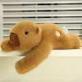 Weighted capybara plush lying on a white ledge with one arm hanging over