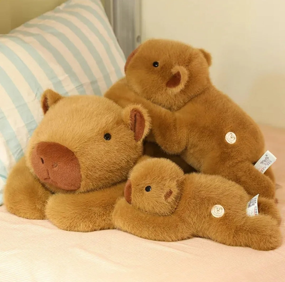 Family of three weighted capybara plushies cuddling on a bed