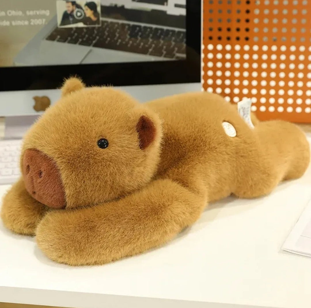 Weighted capybara plush lying down on a desk with arms stretched forward