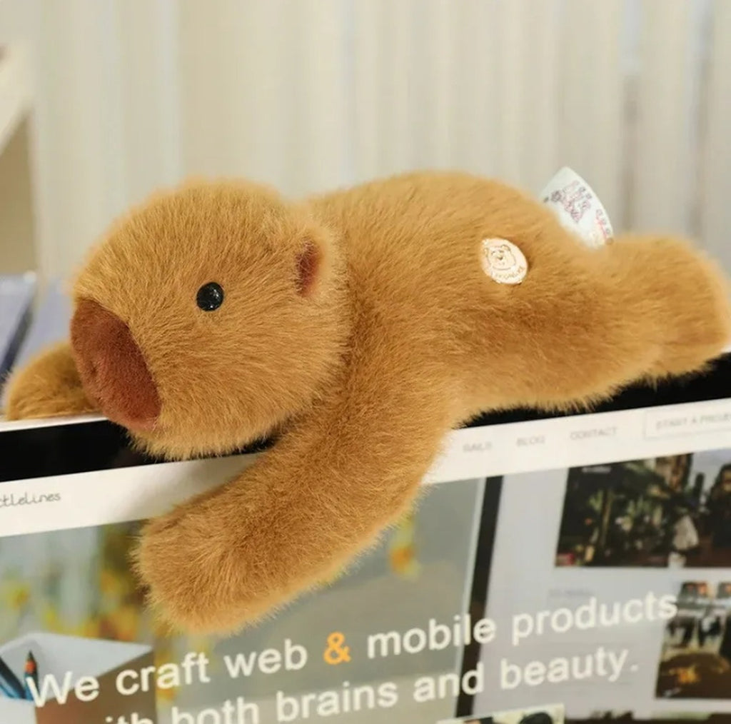 Weighted capybara plush draped over the top of a computer monitor